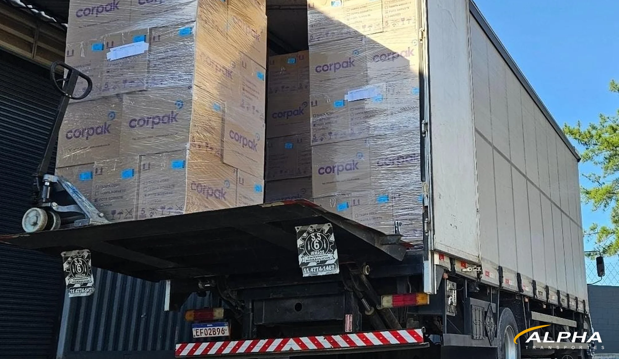 Caminhão da Alpha Transportes com plataforma elevatória carregando pallets de mercadoria