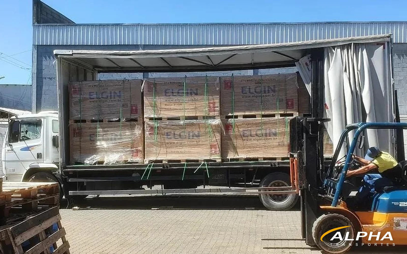 Caminhão sider da Alpha Transportes sendo carregado com empilhadeira em operação